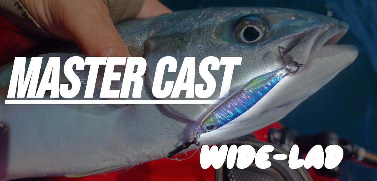 A close-up action shot of a fisherman's hand holding a blue tuna fish with a shiny blue and purple wide-lap cast fishing lure hooked in its mouth. Bold white text overlays read 'MASTER CAST' and 'WIDE-LAD'.